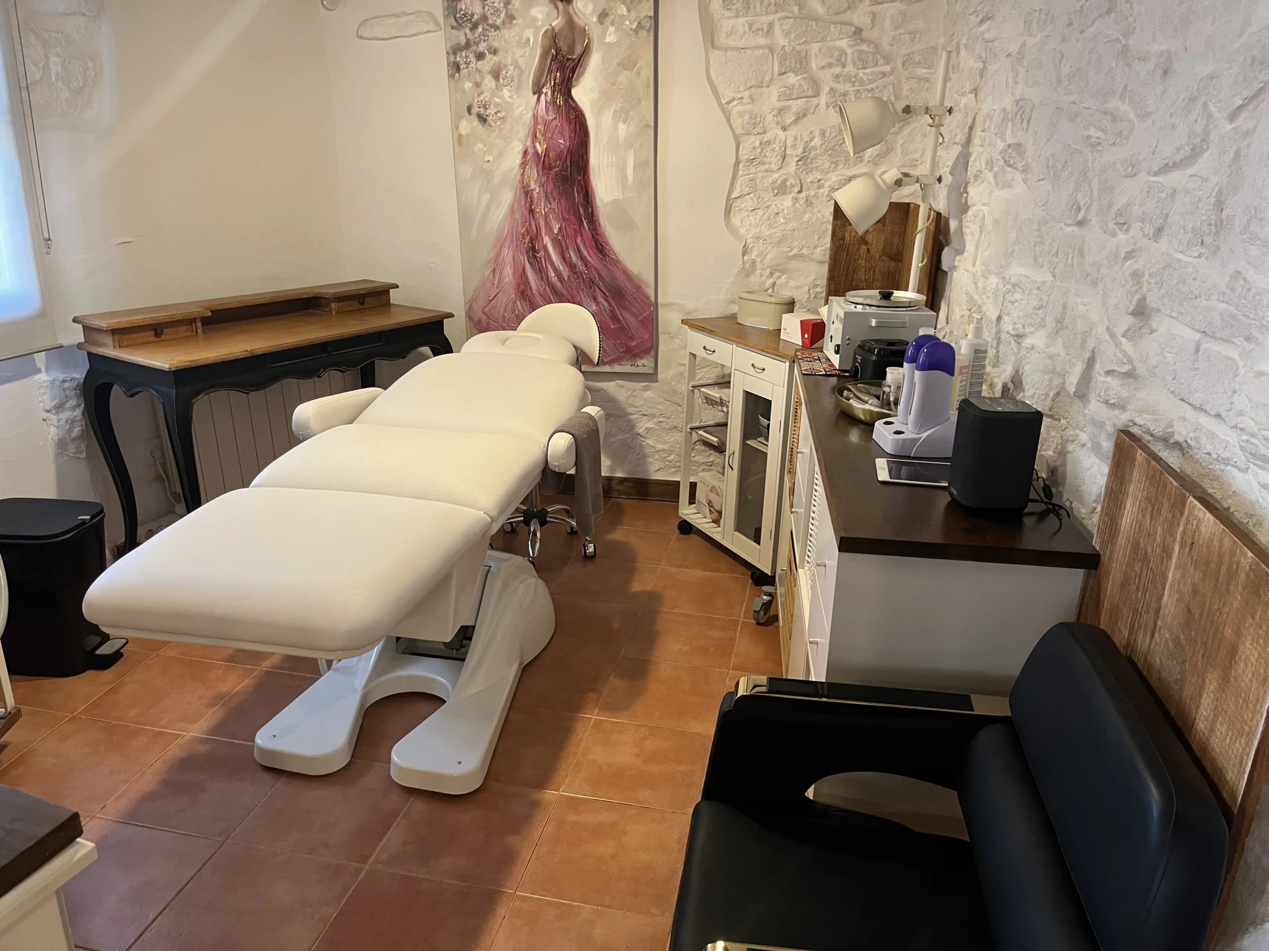 Sala de estética con camilla blanca, decoración elegante y paredes de piedra blanca.