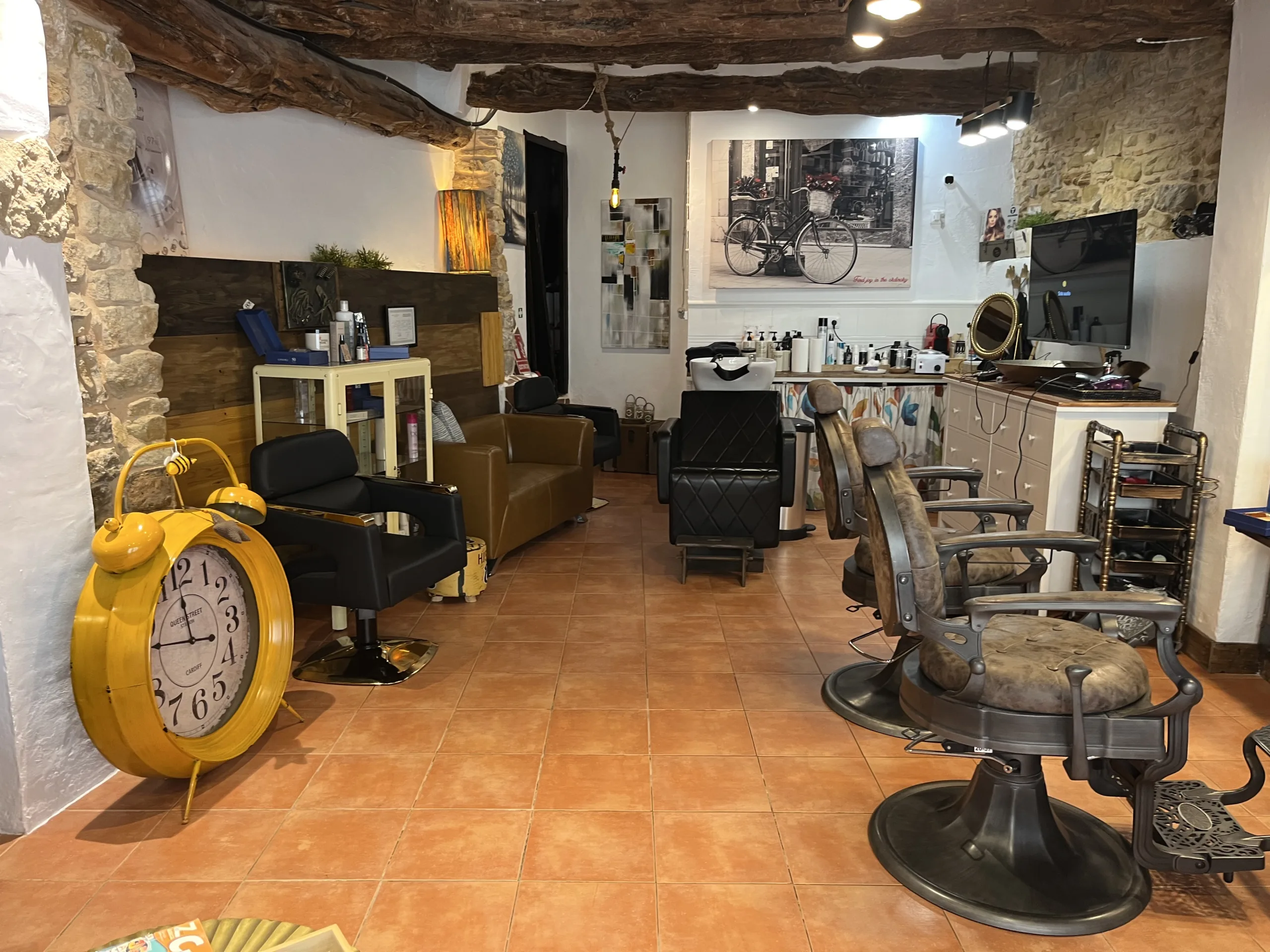 Salón de peluquería con decoración rústica, sillas vintage, productos de cuidado y un gran reloj amarillo decorativo.