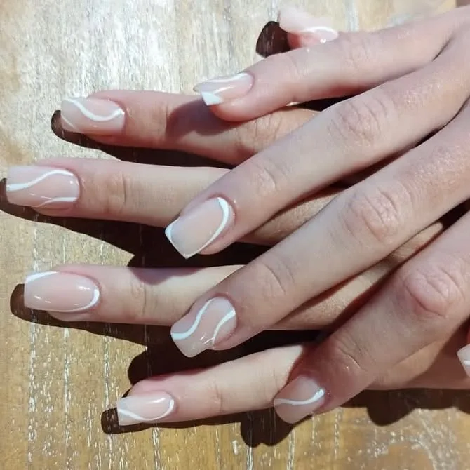 Manicura con uñas largas en tono nude y diseño blanco ondulado.