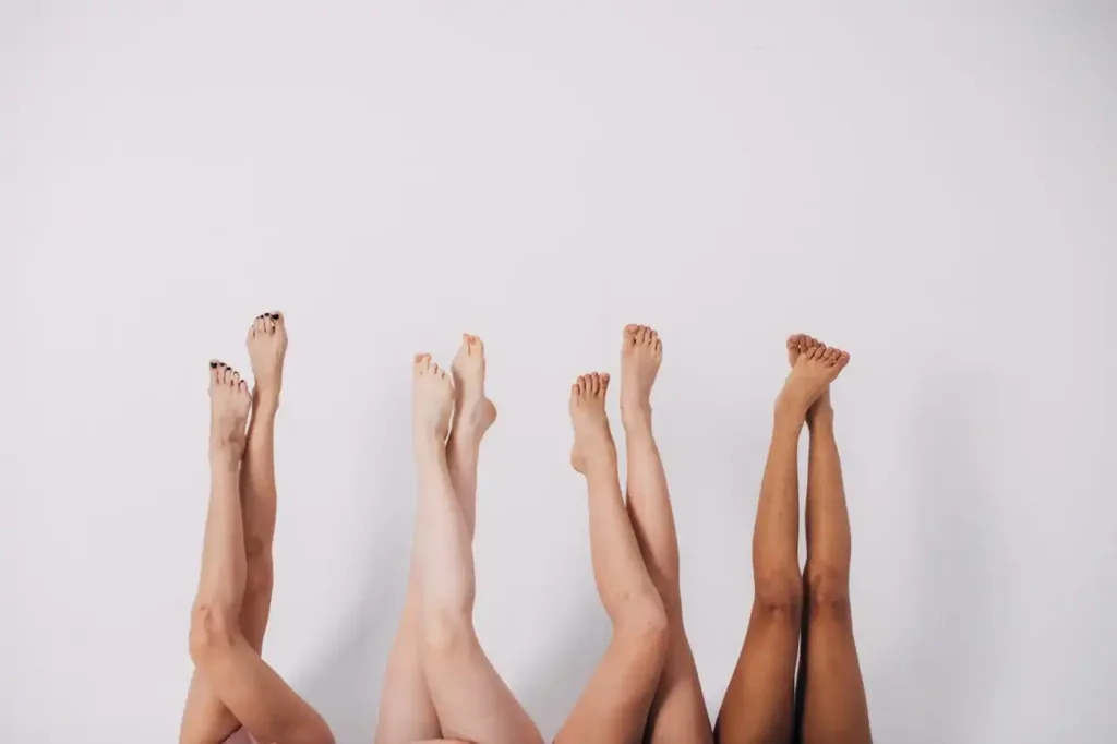 Cuatro pares de piernas alzadas contra una pared blanca, con diferentes tonos de piel.