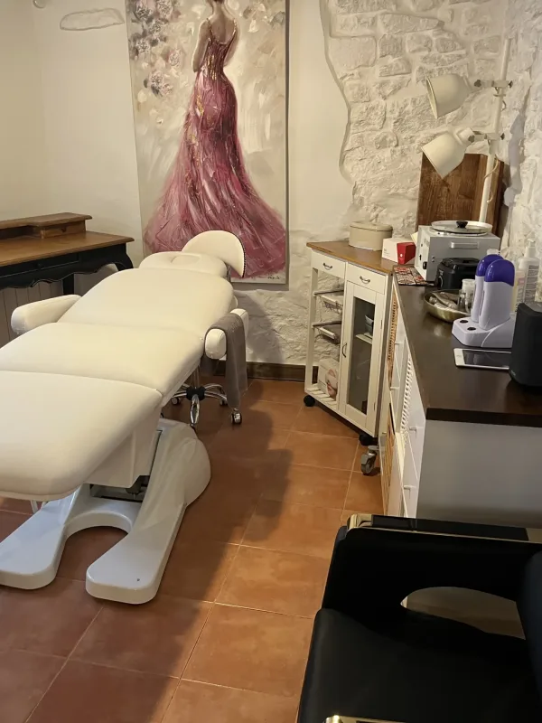 Cabina estética con camilla blanca, mobiliario rústico y decoración con cuadro de vestido rosa.