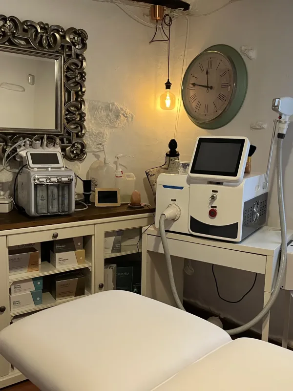 Cabina estética equipada con camilla, maquinaria profesional, espejo decorativo y ambiente acogedor.