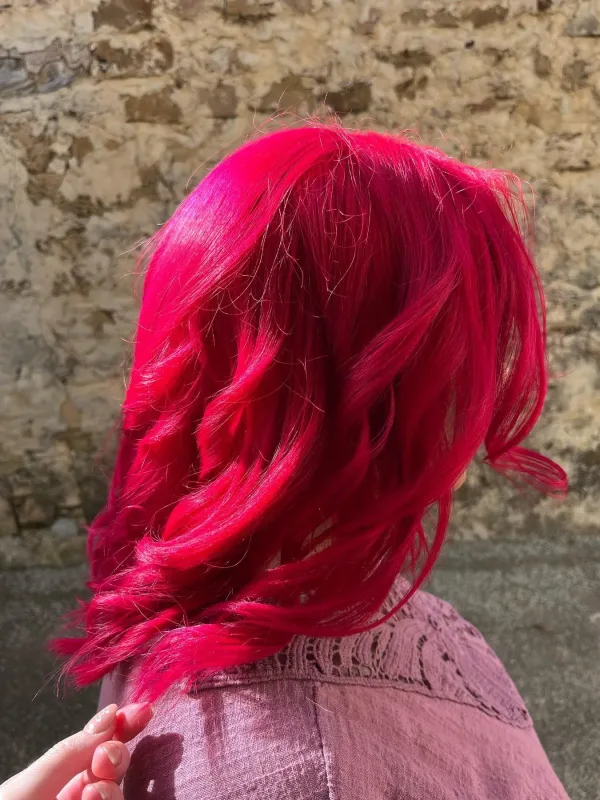 Cabello teñido de rosa intenso con ondas, iluminado por el sol.