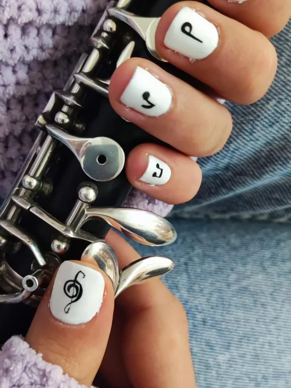 Uñas decoradas con símbolos musicales en esmalte blanco, sujetando un clarinete.