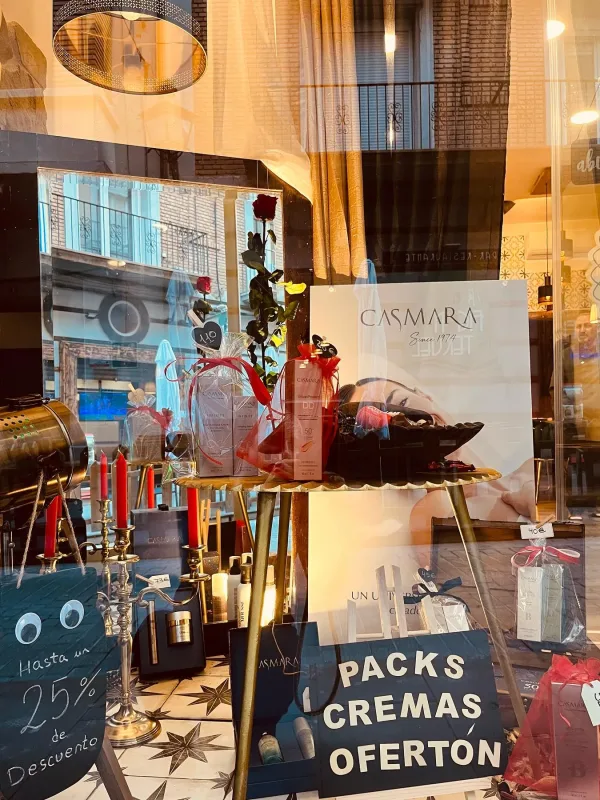Escaparate de tienda de estética con packs de cremas, decoración romántica y cartel de hasta un 25% de descuento.