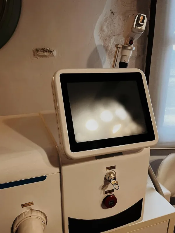 Máquina estética profesional con pantalla apagada y cabezal láser colocado en soporte.